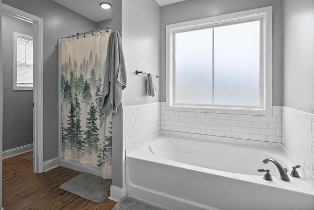 bathroom with a stall shower, a garden tub, baseboards, and wood finished floors