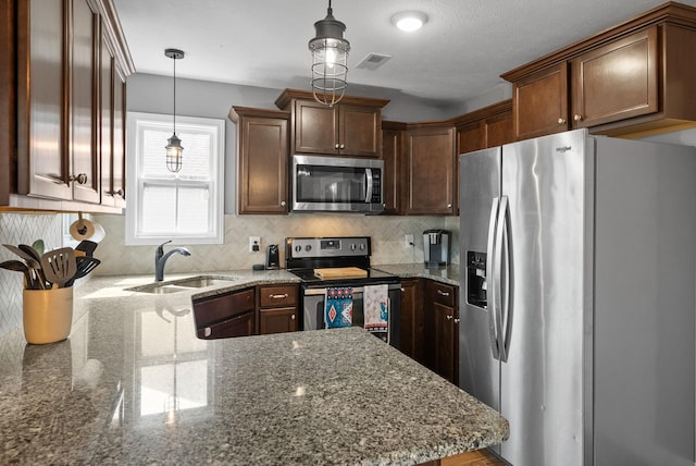 kitchen featuring tasteful backsplash, appliances with stainless steel finishes, a peninsula, pendant lighting, and a sink