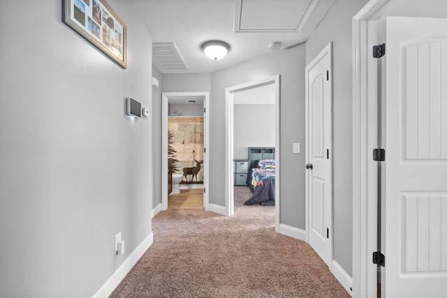 corridor featuring a textured ceiling, carpet, visible vents, and baseboards