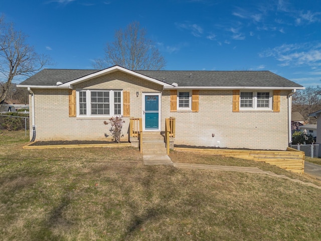 ranch-style home with a front yard, brick siding, fence, and roof with shingles