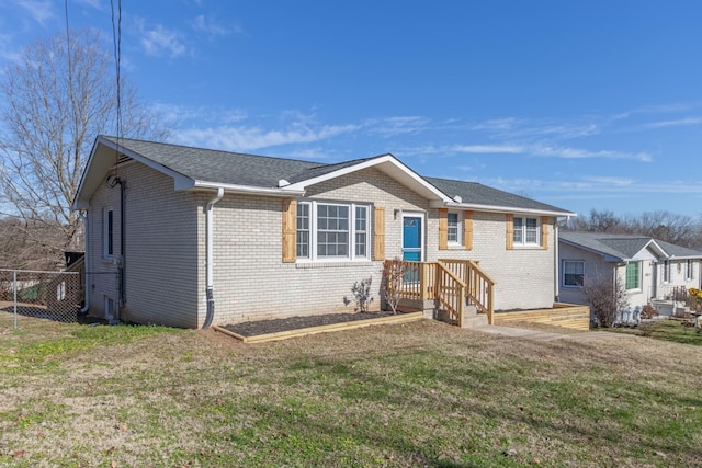 ranch-style house featuring brick siding, roof with shingles, a front yard, and fence