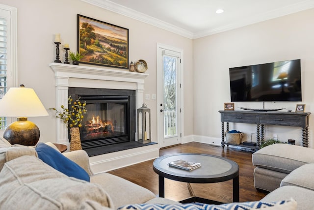 living area featuring recessed lighting, wood finished floors, baseboards, a glass covered fireplace, and crown molding