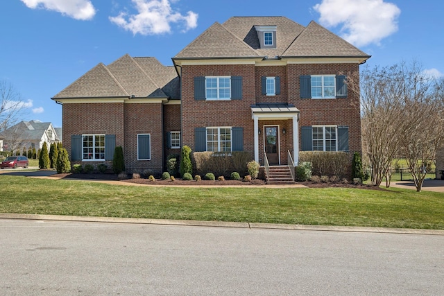 colonial house featuring a shingled roof, a front yard, and brick siding