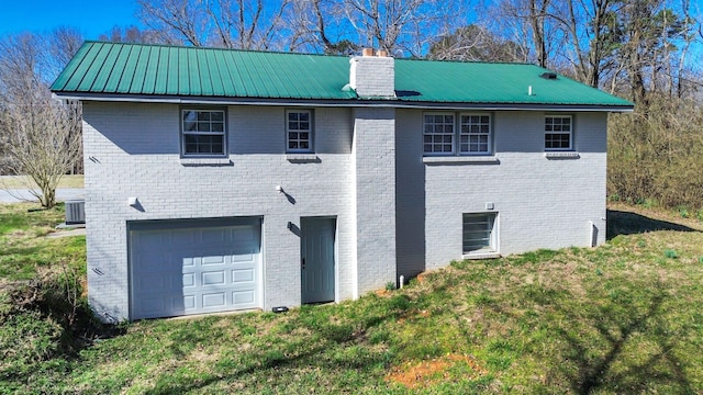 back of house featuring brick siding, metal roof, a chimney, and an attached garage