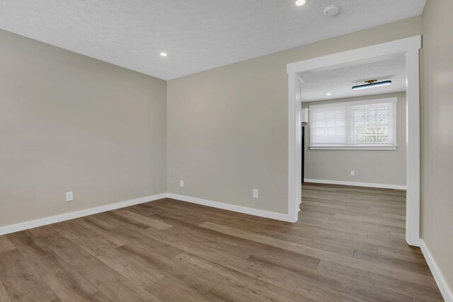 unfurnished room featuring a textured ceiling, baseboards, wood finished floors, and recessed lighting