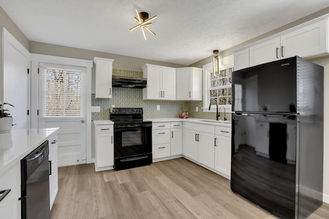 kitchen with light wood-style floors, under cabinet range hood, light countertops, black appliances, and a sink