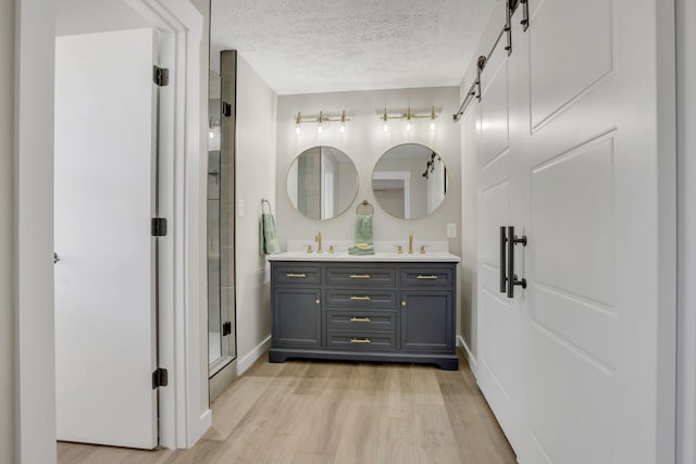 bathroom featuring a textured ceiling, a sink, wood finished floors, a shower stall, and double vanity