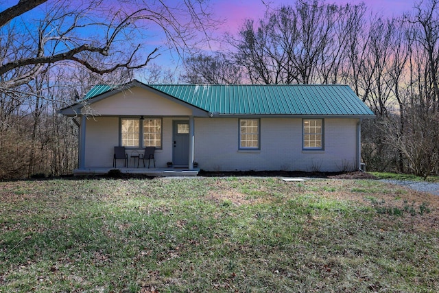 ranch-style home featuring metal roof, a porch, a lawn, and brick siding