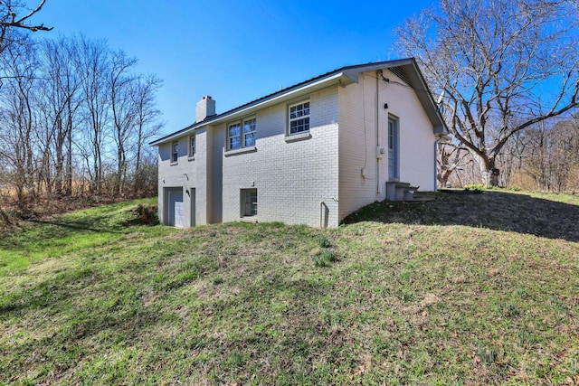 view of side of property with a yard, brick siding, a chimney, and an attached garage