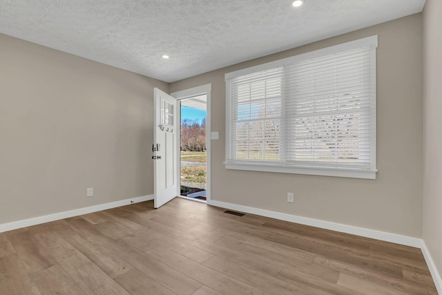 unfurnished room with a textured ceiling, wood finished floors, visible vents, and baseboards