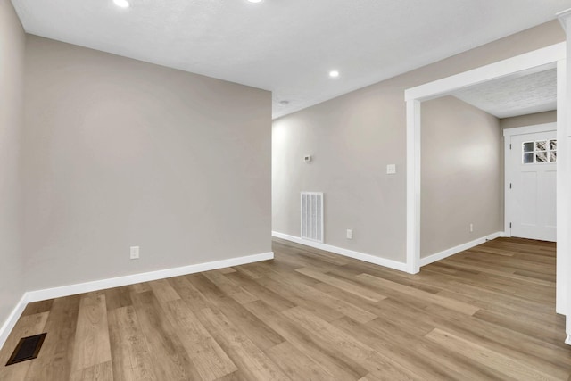 spare room featuring light wood-type flooring, visible vents, and baseboards