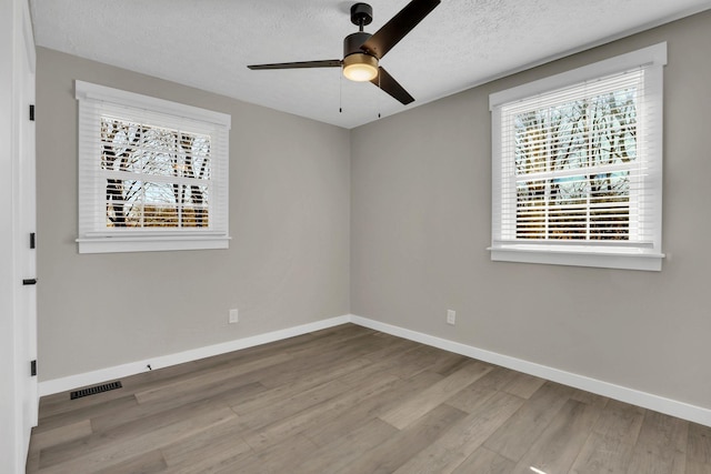 empty room featuring a textured ceiling, wood finished floors, visible vents, and baseboards