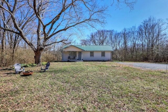 ranch-style house with metal roof, an outdoor fire pit, covered porch, dirt driveway, and a front yard