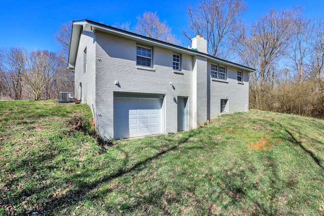 rear view of house with a lawn, a chimney, an attached garage, cooling unit, and brick siding