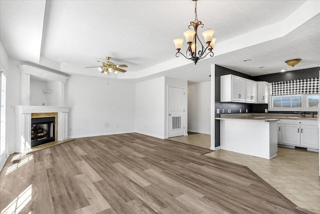 unfurnished living room featuring baseboards, light wood-style flooring, a tray ceiling, a fireplace, and a sink