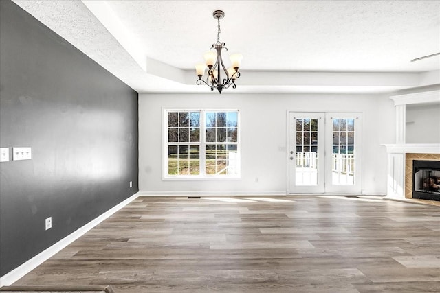 unfurnished dining area featuring baseboards, wood finished floors, a textured ceiling, a notable chandelier, and a high end fireplace