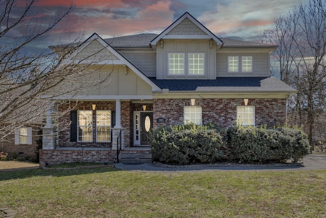 craftsman-style home with brick siding, board and batten siding, a porch, roof with shingles, and a lawn