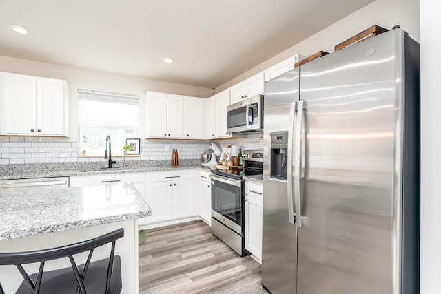 kitchen with appliances with stainless steel finishes, a sink, white cabinetry, and tasteful backsplash