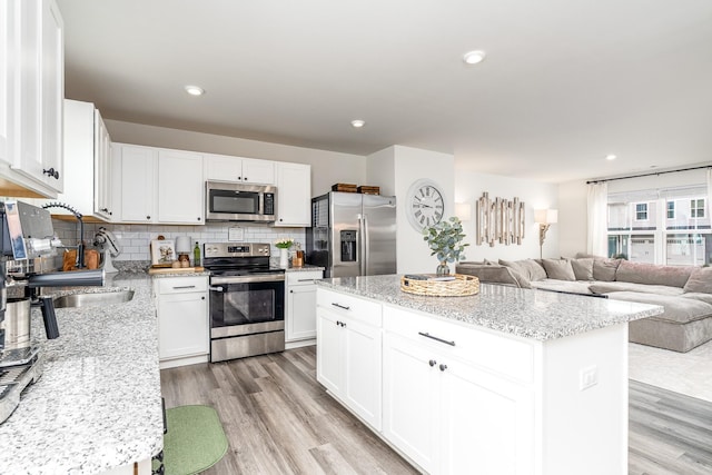 kitchen featuring appliances with stainless steel finishes, backsplash, a sink, and light wood-style floors