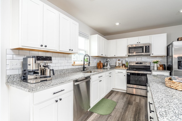 kitchen with light stone counters, dark wood-style flooring, a sink, white cabinetry, and appliances with stainless steel finishes