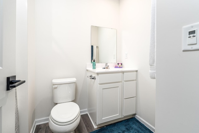 half bathroom featuring baseboards, vanity, toilet, and wood finished floors