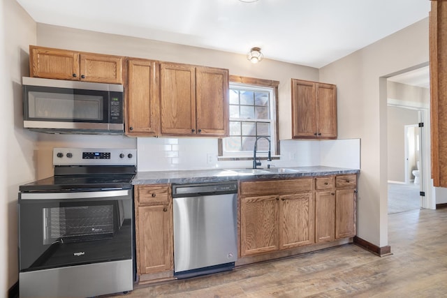 kitchen featuring stainless steel appliances, baseboards, a sink, light wood finished floors, and brown cabinetry