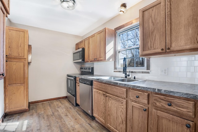 kitchen with light wood-type flooring, backsplash, a sink, dark countertops, and appliances with stainless steel finishes