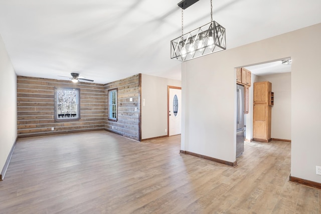 unfurnished living room featuring baseboards, light wood-style flooring, wood walls, and ceiling fan