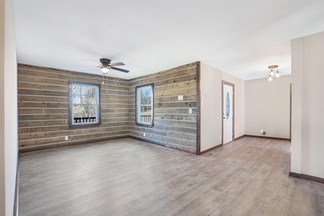 unfurnished living room with a ceiling fan, baseboards, wooden walls, and wood finished floors