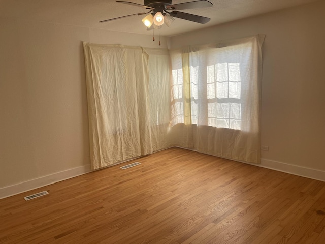 spare room featuring baseboards, visible vents, ceiling fan, and wood finished floors