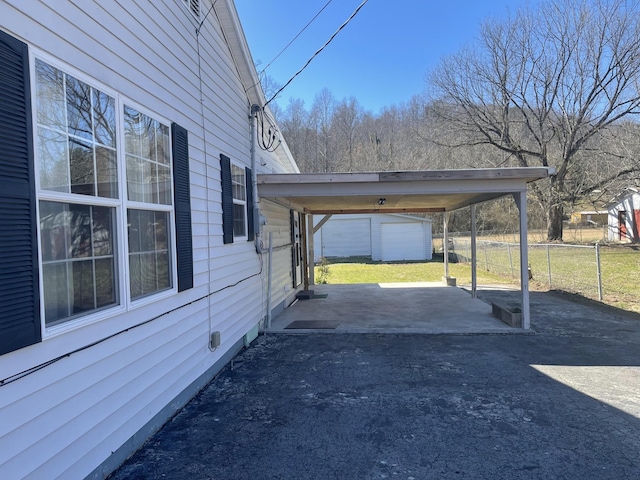 view of parking with aphalt driveway, fence, and a carport