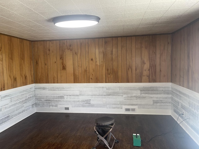 empty room featuring wood walls, visible vents, and wood finished floors