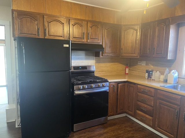 kitchen with stainless steel gas stove, dark wood finished floors, freestanding refrigerator, light countertops, and under cabinet range hood