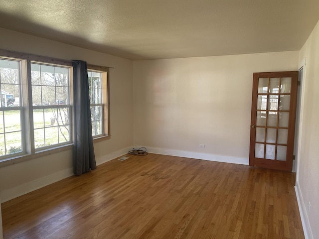 empty room with a textured ceiling, wood finished floors, visible vents, and baseboards