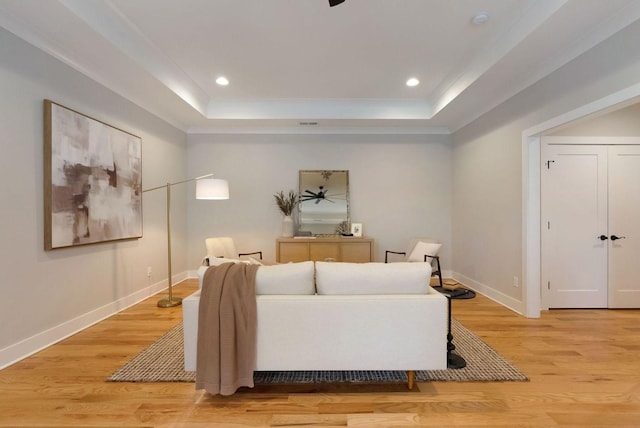 living area with light wood-style flooring, baseboards, and a raised ceiling