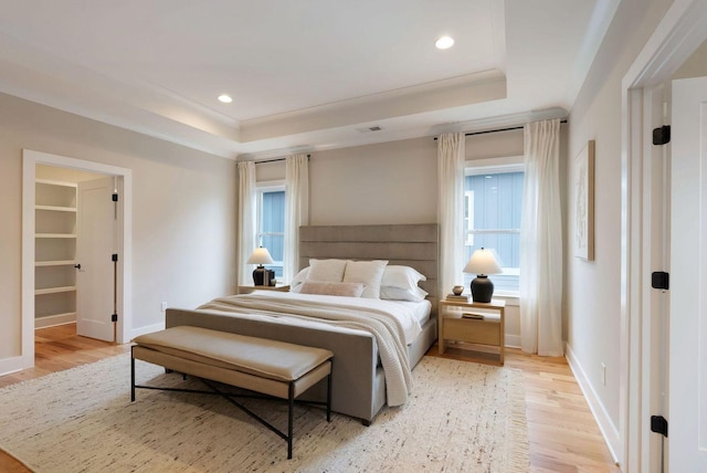 bedroom featuring light wood finished floors, multiple windows, a raised ceiling, and baseboards