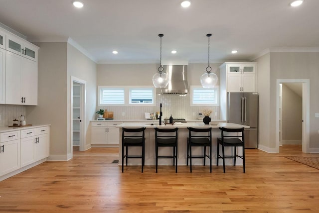 kitchen with light countertops, light wood-style flooring, high quality fridge, wall chimney range hood, and a kitchen bar