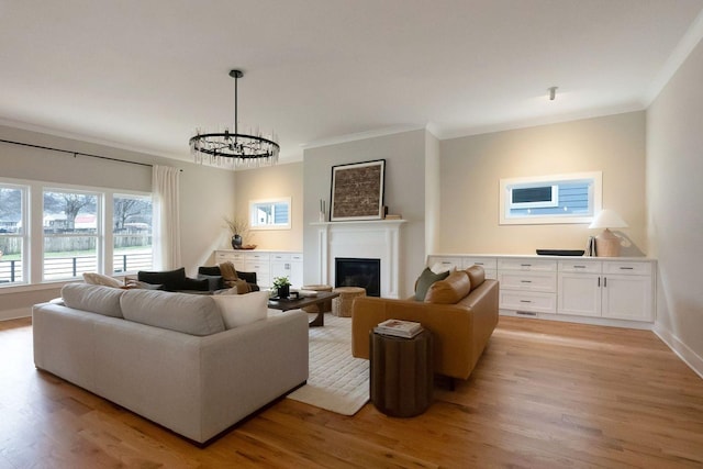 living room with crown molding, a glass covered fireplace, and light wood-style floors