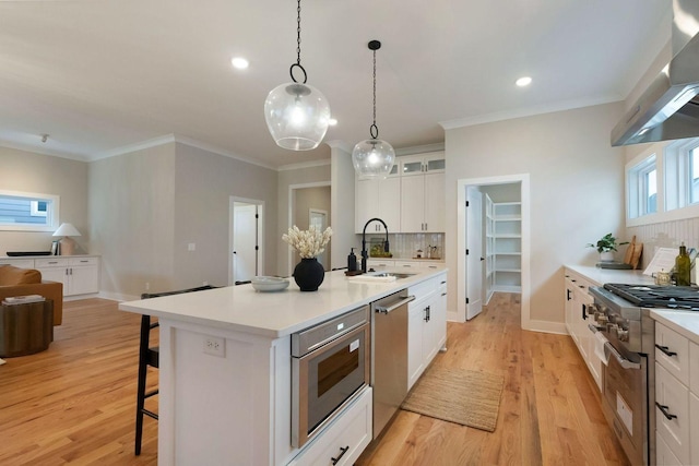 kitchen with a breakfast bar area, a sink, appliances with stainless steel finishes, wall chimney exhaust hood, and tasteful backsplash