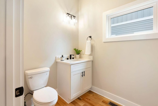 half bath with vanity, wood finished floors, toilet, and baseboards