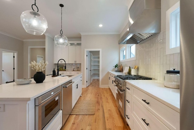 kitchen with stainless steel appliances, crown molding, a sink, and wall chimney range hood