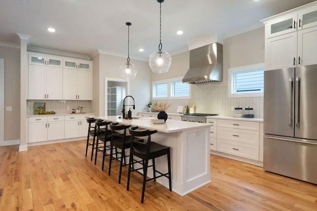 kitchen featuring wall chimney exhaust hood, high quality fridge, ornamental molding, a kitchen breakfast bar, and light countertops