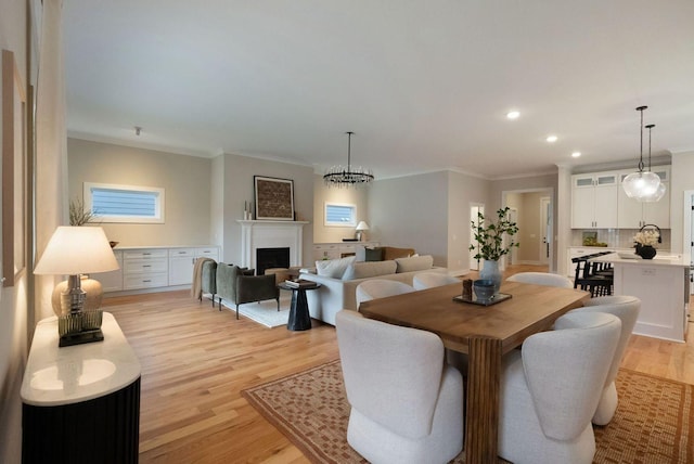 dining area with ornamental molding, light wood finished floors, a fireplace, and recessed lighting