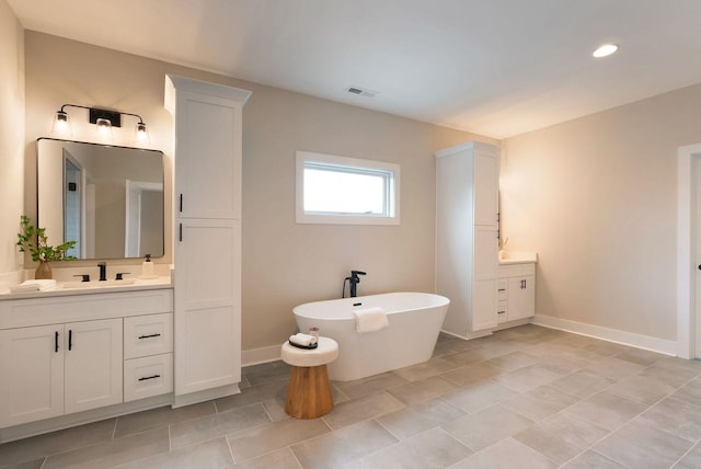 bathroom featuring a freestanding tub, two vanities, a sink, visible vents, and baseboards