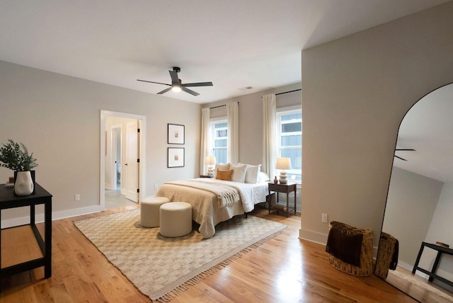 bedroom with arched walkways, ceiling fan, wood finished floors, and baseboards