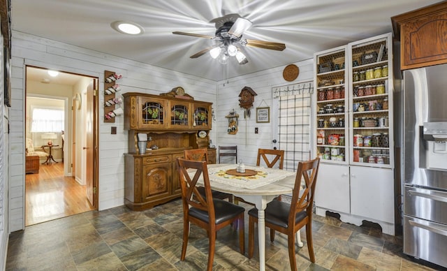 dining room with ceiling fan, wooden walls, and stone finish floor