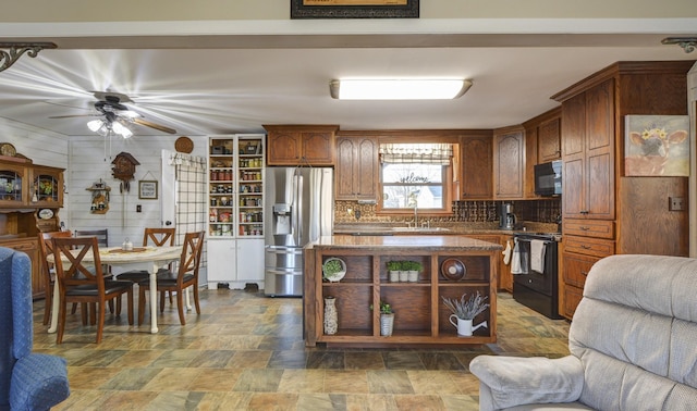 kitchen featuring a sink, open floor plan, black appliances, tasteful backsplash, and stone finish floor