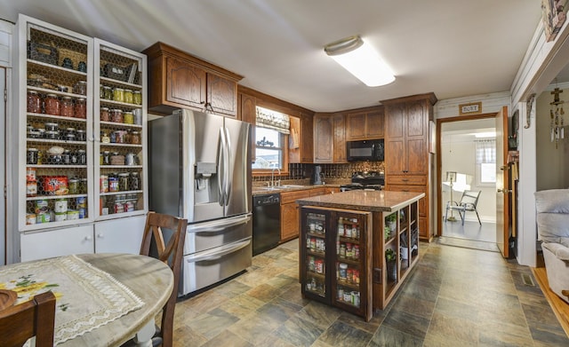 kitchen with black appliances, stone finish floor, a wealth of natural light, and decorative backsplash