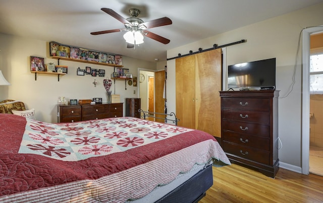 bedroom with a barn door, baseboards, a ceiling fan, wood finished floors, and ensuite bathroom