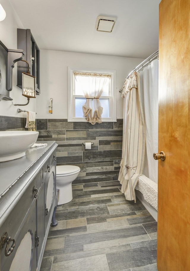 full bath featuring curtained shower, toilet, vanity, tile walls, and wainscoting